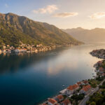 Vue aérienne de la Baie de Kotor, Monténégro, avec villages côtiers, montagnes luxuriantes et eaux calmes sous un ciel clair.