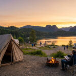 Camping au bord d'un lac au coucher du soleil avec tente, feu de camp, couple, et VR. Montagnes et forêts en arrière-plan.