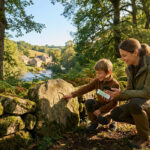 Une mère et son enfant en forêt. L'enfant pointe une rose des vents sculptée sur une pierre, la mère tient un smartphone avec une carte.
