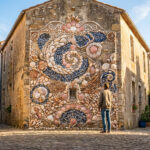 Homme admirant une façade décorée d'une grande fresque murale de coquillages colorés dans une ruelle ensoleillée.