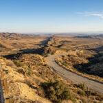 Vue aérienne de la faille de San Andreas s'étendant dans un paysage désertique californien avec une route sinueuse et un homme.