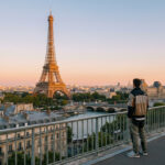 Un homme de dos admire la Tour Eiffel et le Louvre depuis un pont à Paris au coucher du soleil.