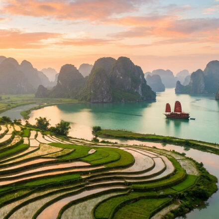 Que faire au Vietnam en 2026 : les lieux à voir absolument Vue aérienne d'un paysage vietnamien au coucher du soleil. Rizières en terrasses, rivière, karsts calcaires et jonque à voile rouge.