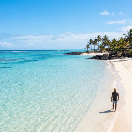 Voyage à l’île Maurice : mes conseils et astuces essentiels Un homme marche sur une plage de sable blanc bordée de palmiers, face à une mer turquoise et limpide à l'île Maurice.