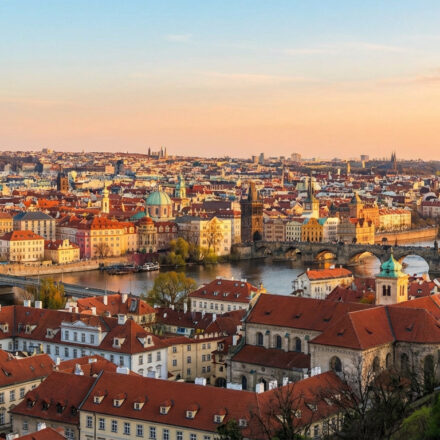 Panorama de Prague au crépuscule. La Vltava serpente entre les bâtiments aux toits rouges, dominés par l'Église du Týn et le Pont Charles.